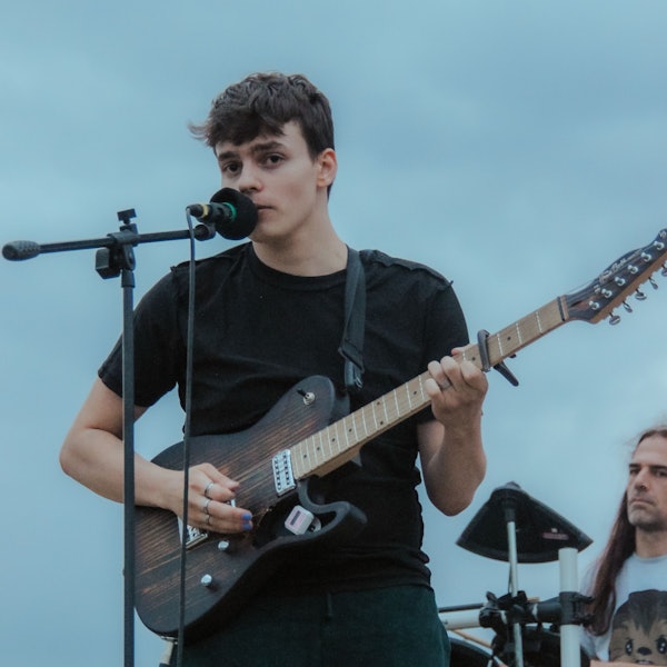 Ein junger Mann steht mit einer Gitarre an einem Mikrofon.