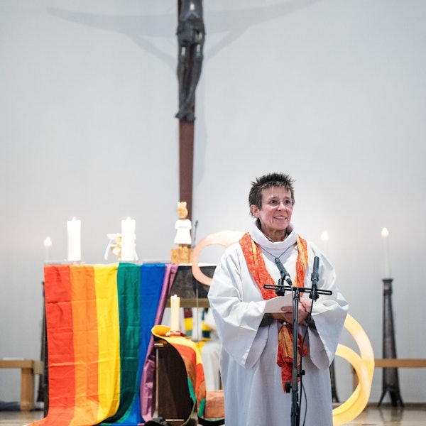 Marianne Arndt steht vor einem Altar mit Regenbogenflagge