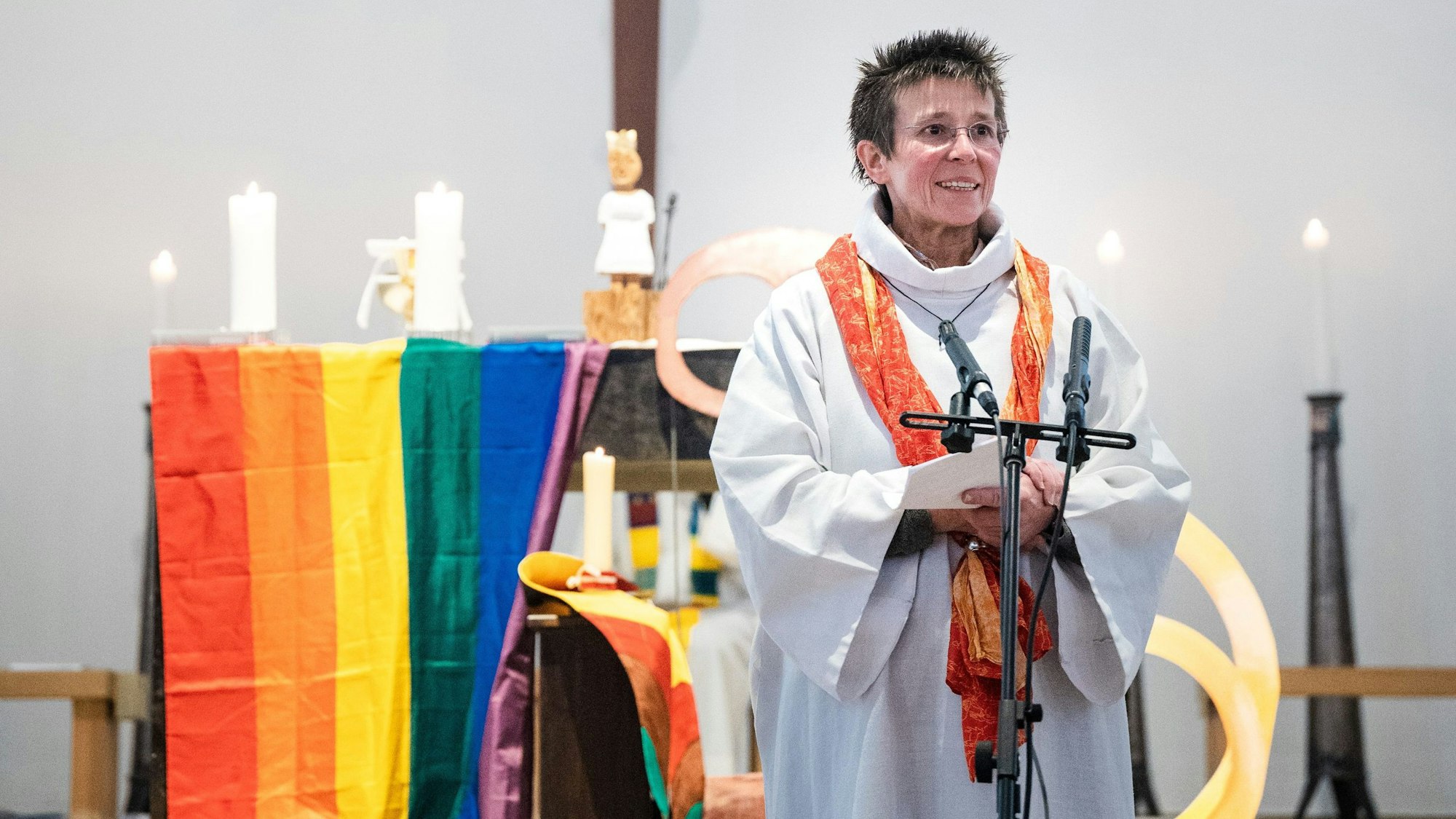 Marianne Arndt steht vor einem Altar mit Regenbogenflagge