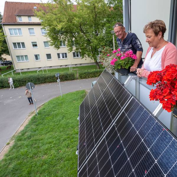 Zwei Mieter blicken über die Module ihres neuen Balkonkraftwerkes am Balkon ihrer Wohnung.