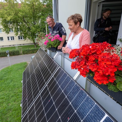Zwei Mieter blicken über die Module ihres neuen Balkonkraftwerkes am Balkon ihrer Wohnung.