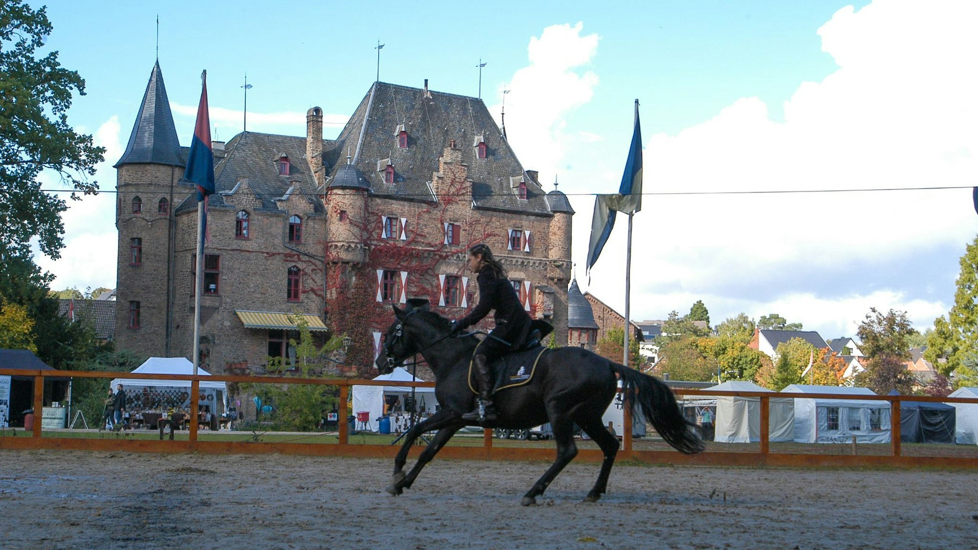 Patricia Gräfin Beissel reitet bei den Ritterspielen auf einem schwarzen Pferd. Im Hintergrund ist ihre Burg Satzvey zu sehen.