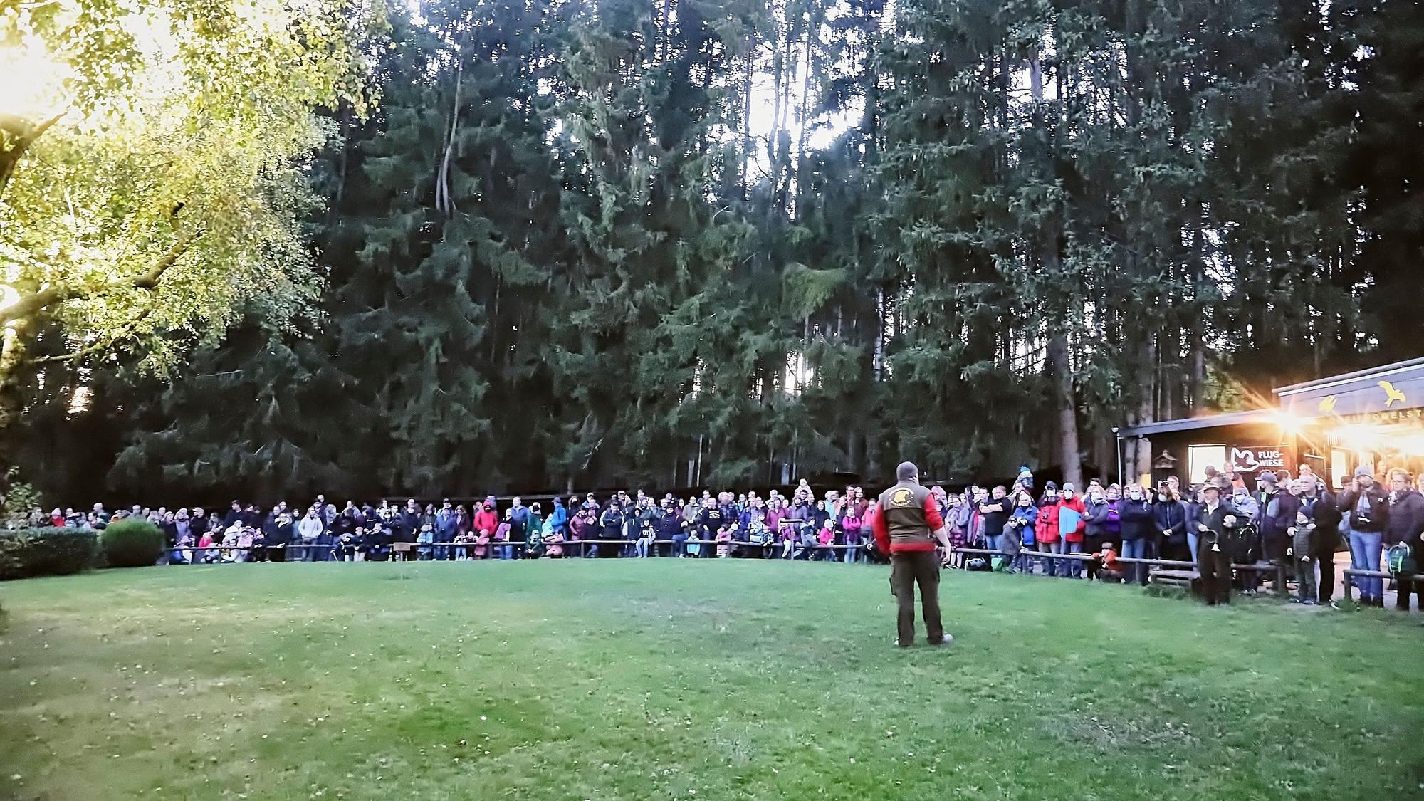 Ein Mann steht in der Abendsonne auf einer Wiese, um die sich ein großes Publikum versammelt hat.