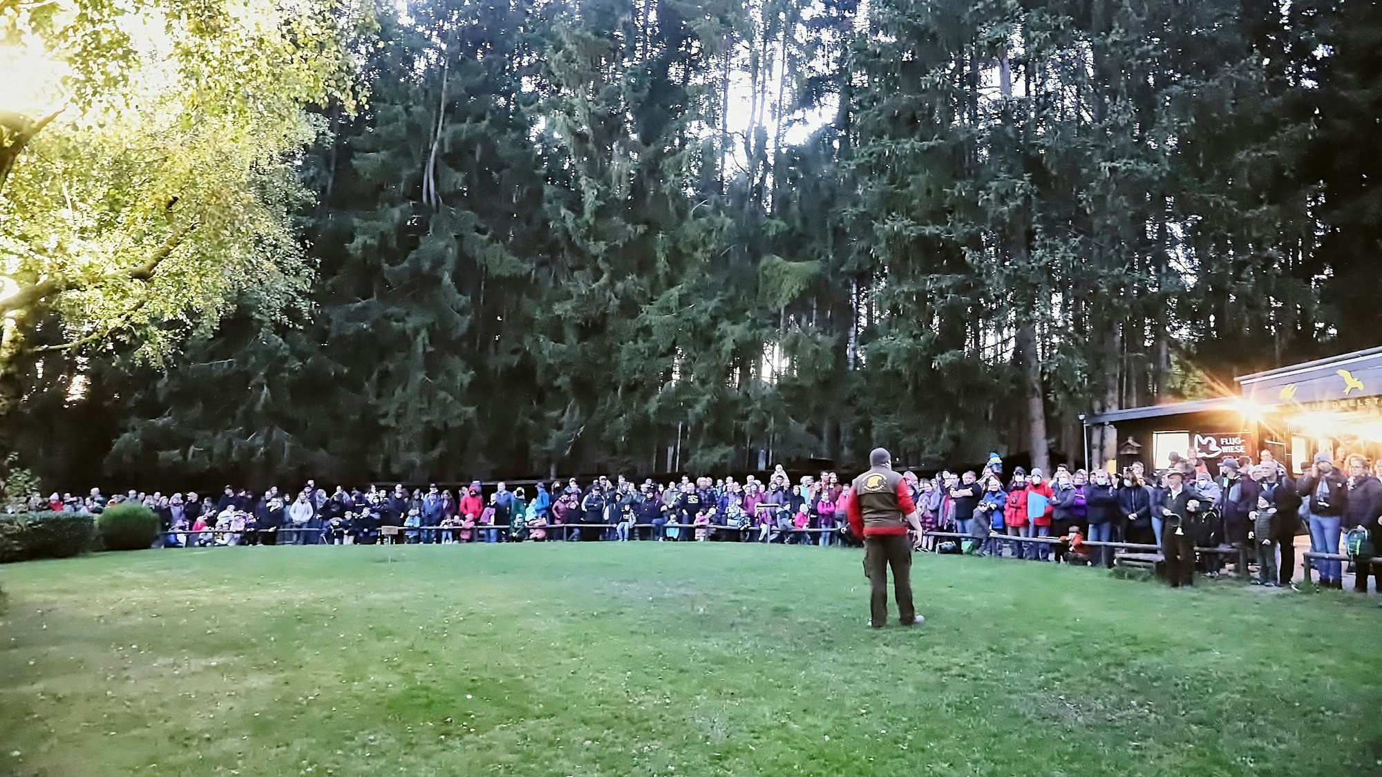 Ein Mann steht in der Abendsonne auf einer Wiese, um die sich ein großes Publikum versammelt hat.