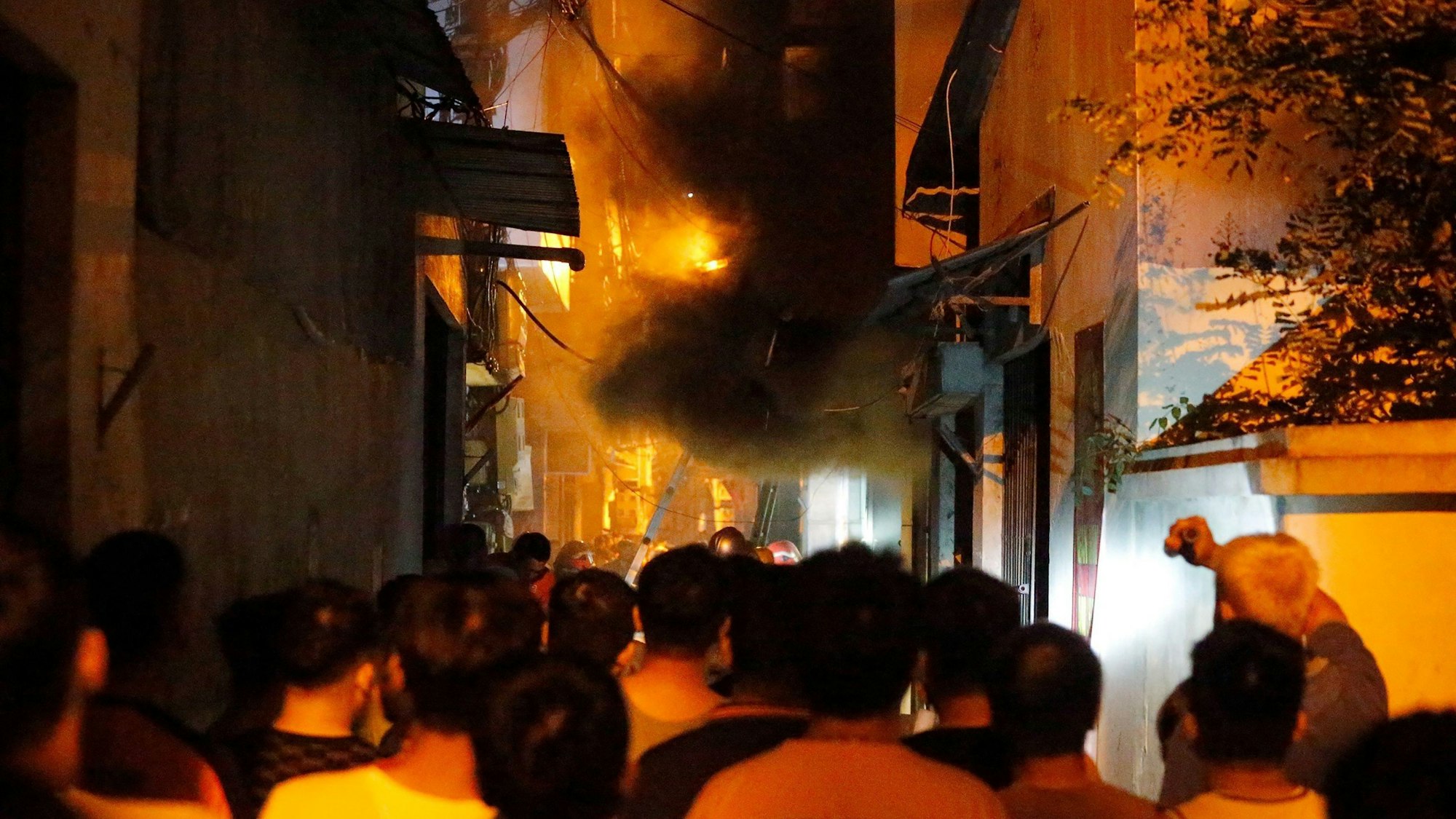 Menschen auf der Straße schauen das brennende Wohnhaus in Hanoi an.
