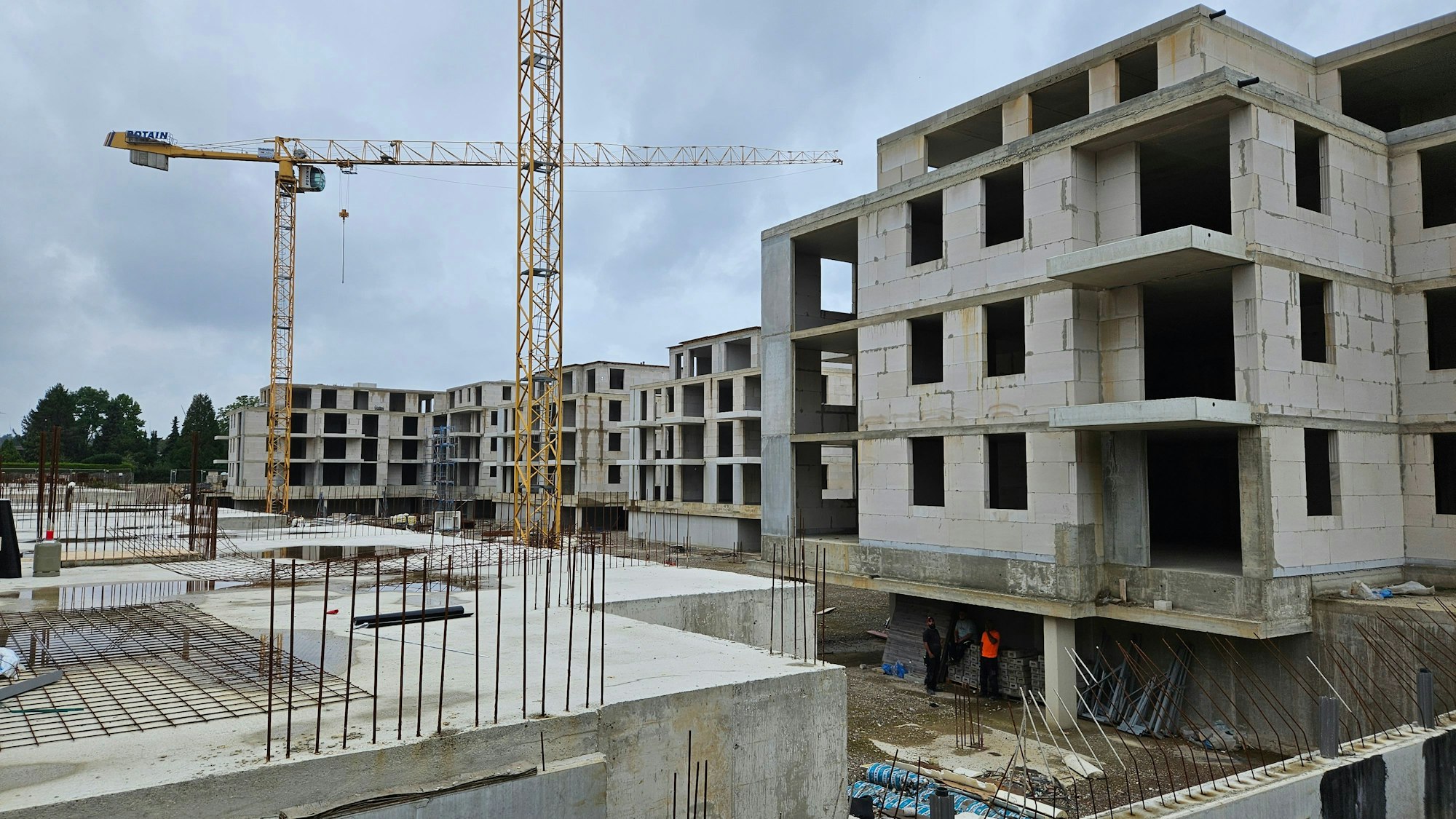 Zwei Kräne stehen vor nackten und mehrstöckigen Rohbauten.