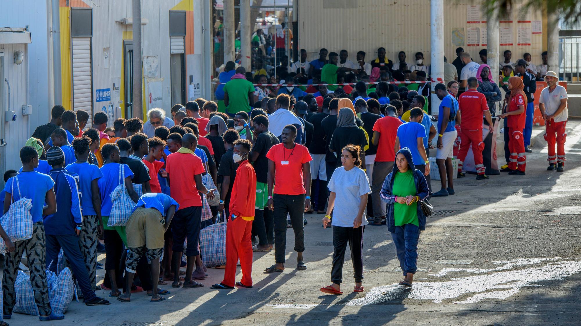Migranten stehen vor Gebäuden auf der Insel Lampedusa.