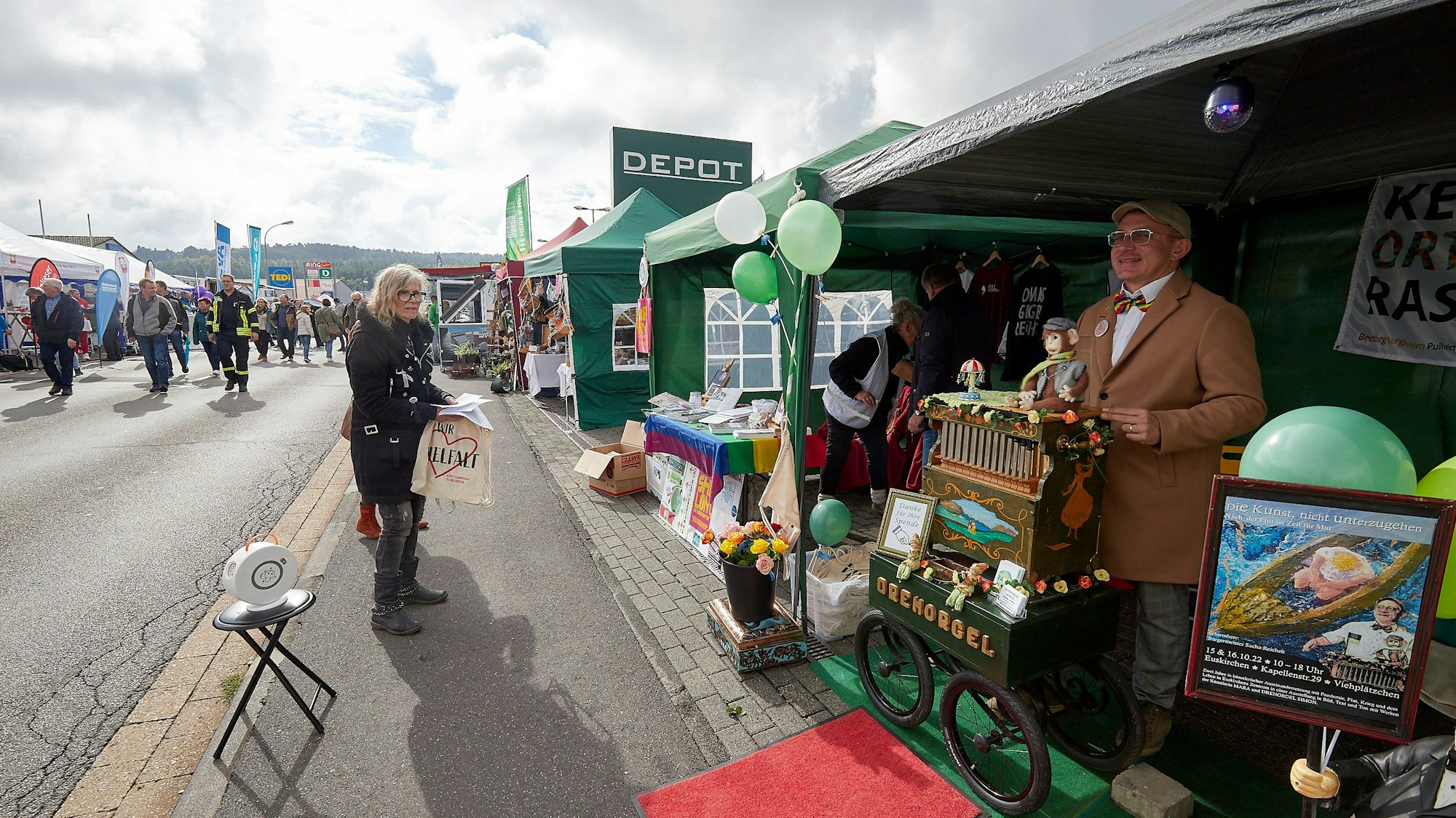 Verschiedene Stände sind entlang einer Straße aufgebaut, rechts steht ein Mann an einer herbstlich dekorierten Drehorgel.