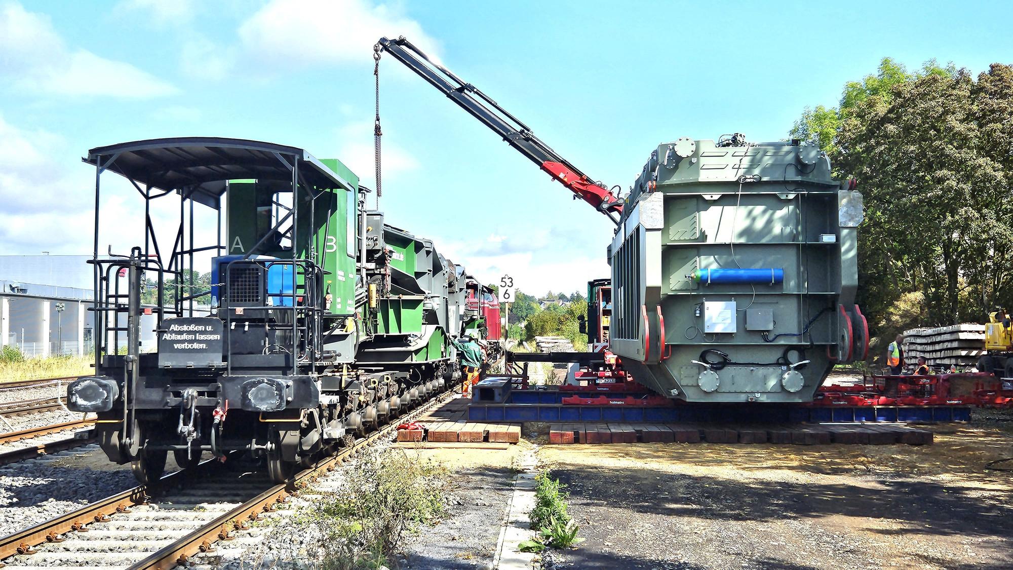 Ein Trafo (r.) für die Umspannanlage Dahlem ist am Bahnhof Kall angekommen und mit einem Kran vom Waggon abgeladen worden.