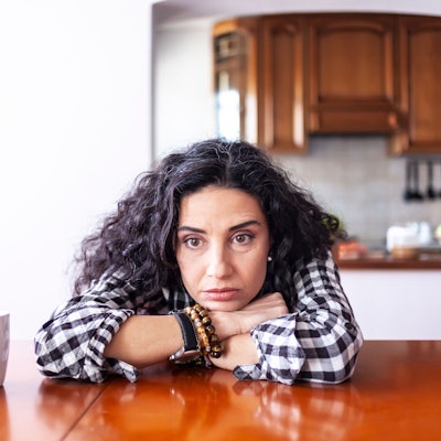 Frau sitzt zu Hause und sorgt sich, dass ihr Mann sie betrügt. Symbolbild