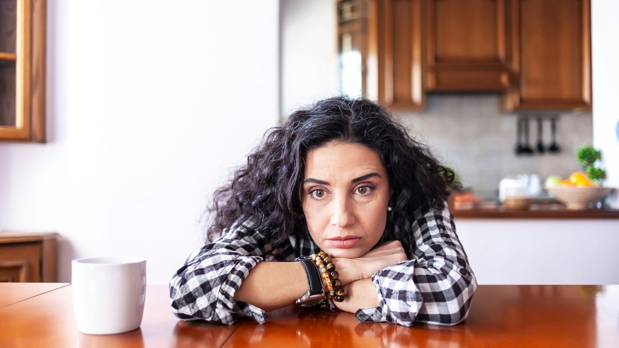 Frau sitzt zu Hause und sorgt sich, dass ihr Mann sie betrügt. Symbolbild