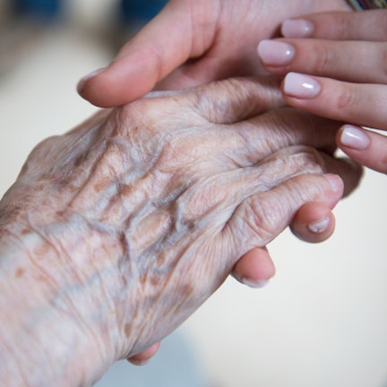 Eine Pflegerin hält die Hand einer Seniorin.