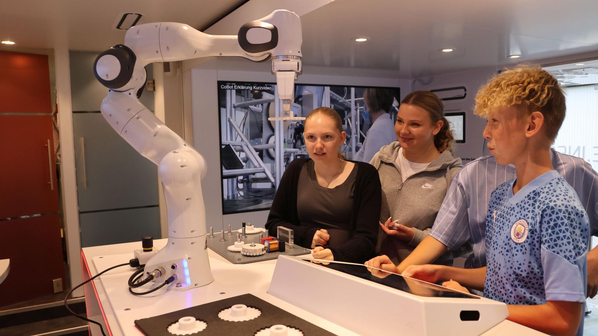 Drei Schüler bedienen über ein Eingabefeld den Arm eines Roboters.