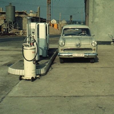 Anfang der 60er Jahre in Troisdorf. Ein Auto steht an einer Tankstelle ohne Überdachung, im Hintergrund sieht man eine Baustelle.