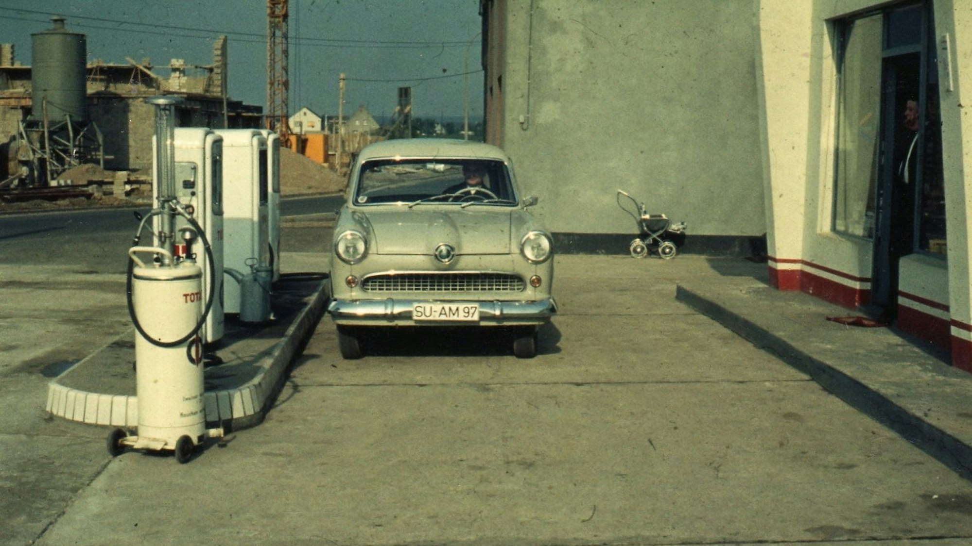 Anfang der 60er Jahre in Troisdorf. Ein Auto steht an einer Tankstelle ohne Überdachung, im Hintergrund sieht man eine Baustelle.