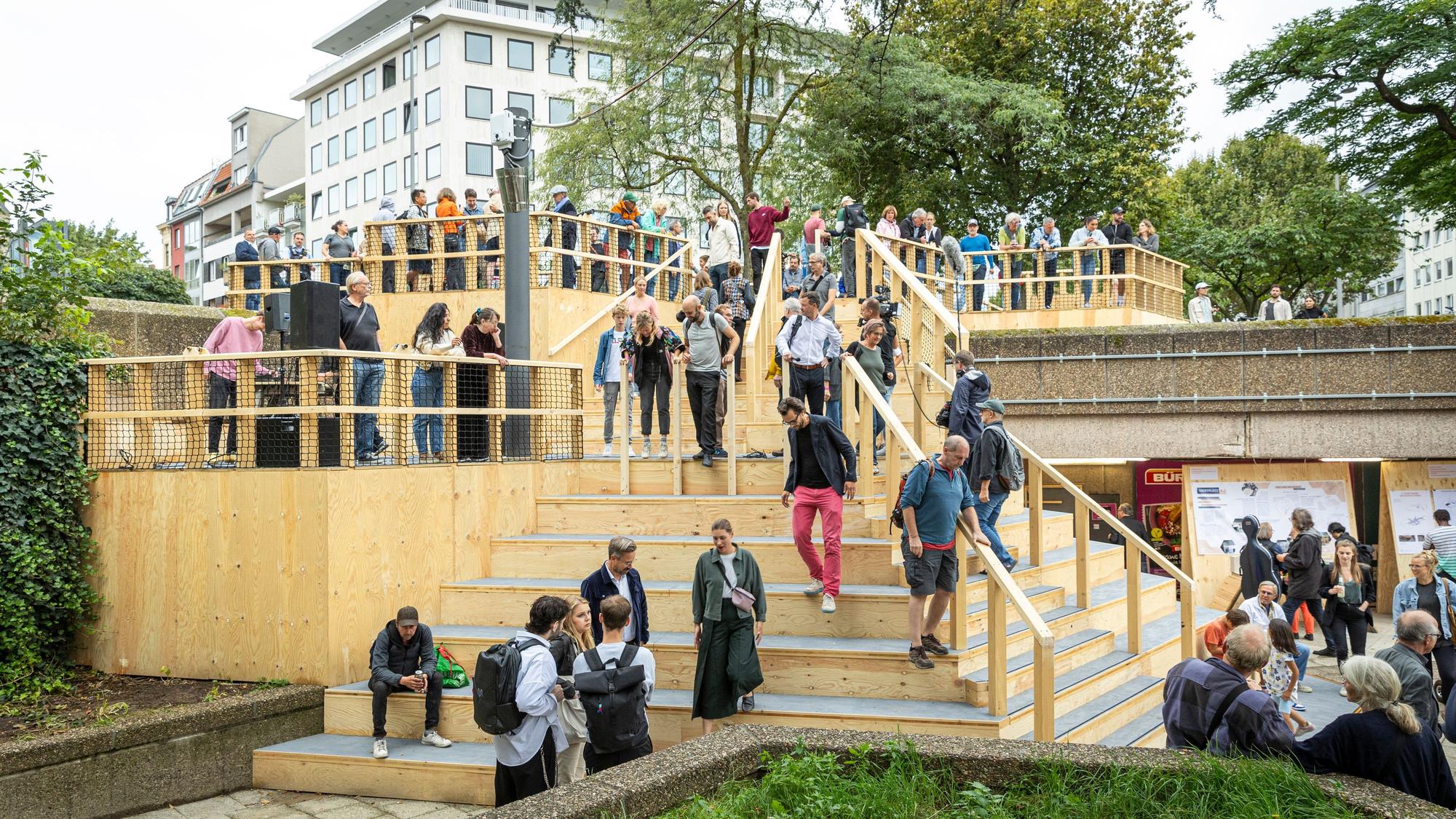 Personen laufen die Freitreppe aus Holz hoch und runter.