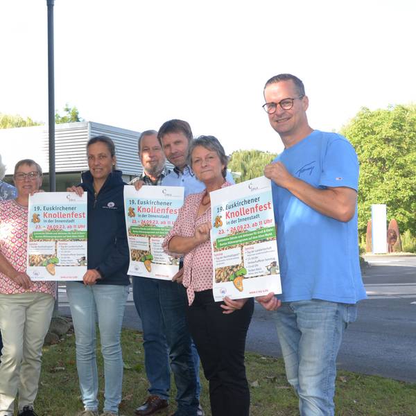 Acht Frauen und Männer, die das Euskirchener Knollenfest vorbereiten, stehen in einer Reihe. Sie zeigen Werbeplakate für die Großveranstaltung.