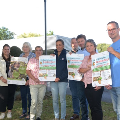 Acht Frauen und Männer, die das Euskirchener Knollenfest vorbereiten, stehen in einer Reihe. Sie zeigen Werbeplakate für die Großveranstaltung.
