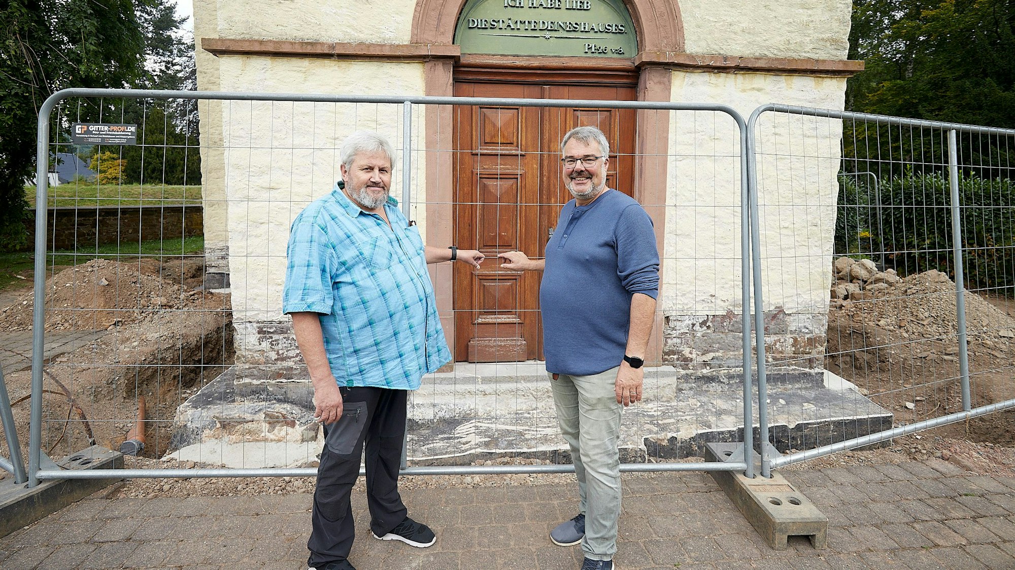Zwei Männer stehen vor dem mit einem Bauzaun abgesperrten Portal der Kirche in Schleiden.