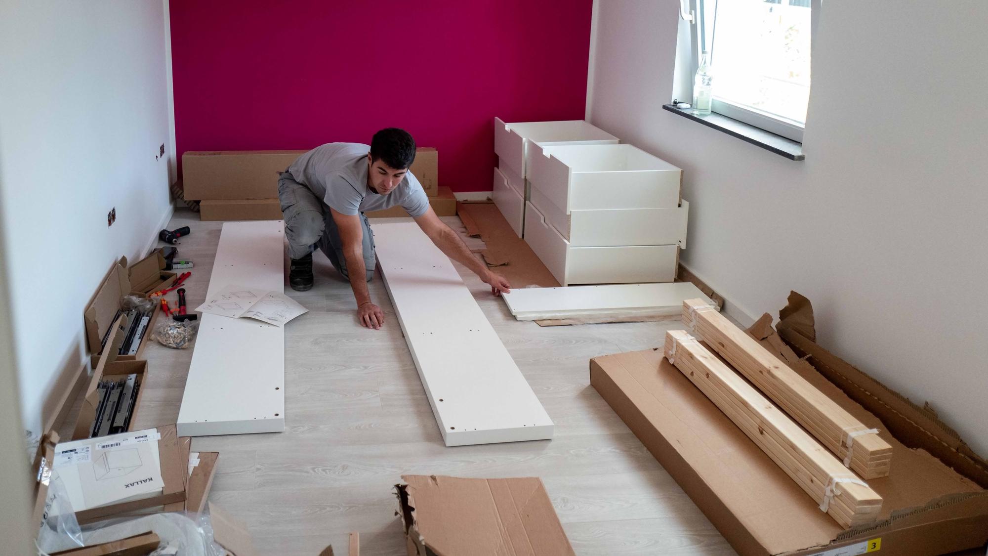 Das Bild zeigt einen Handwerker, wie er einen Schrank zusammenbaut.