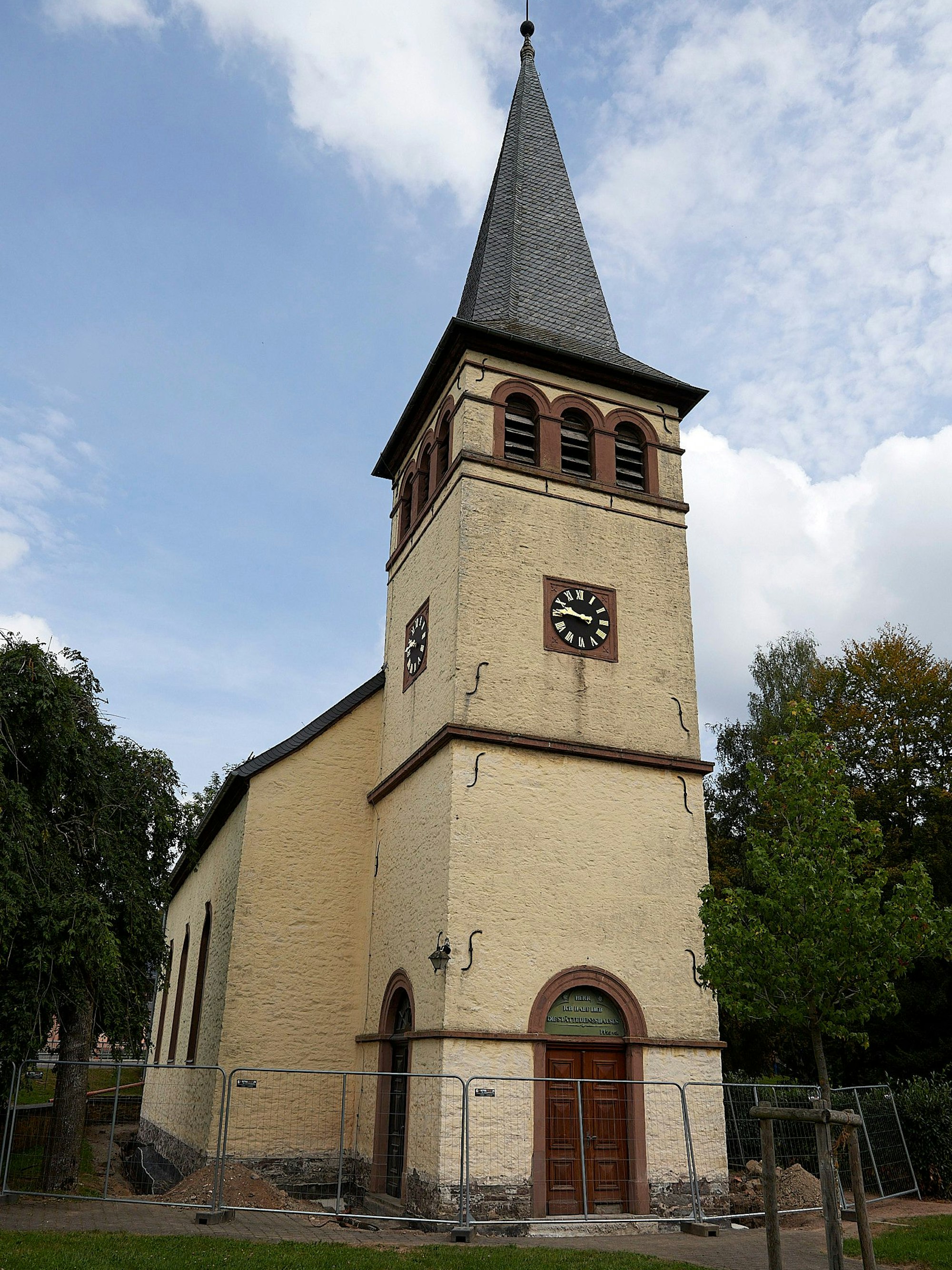 Ein Bauzaun ist ringsum eine gelb angestrichene Kirche aufgestellt.