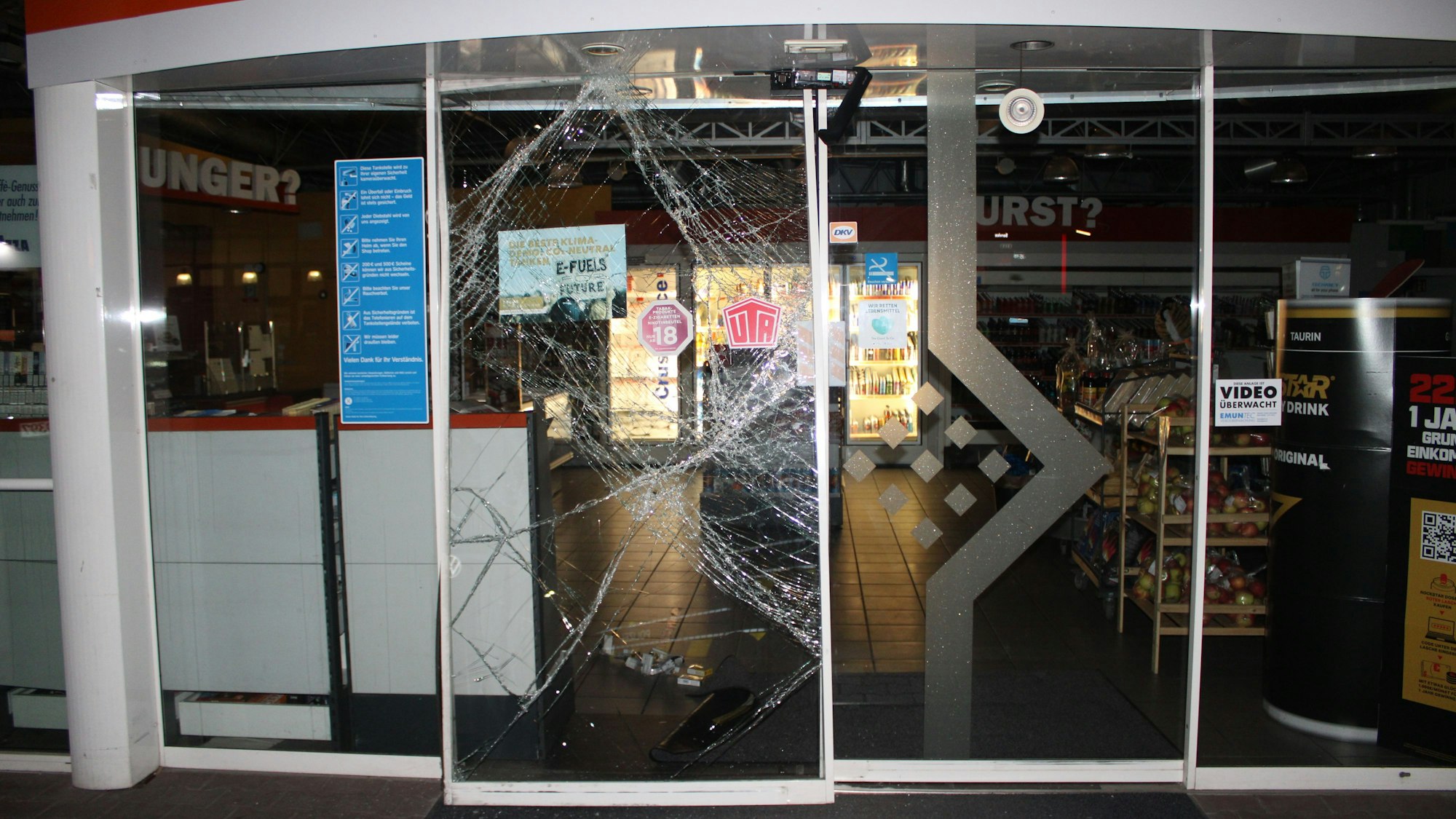 Auf einer Nachtaufnahme ist das zerborstene Glas einer Eingangstür einer Tankstelle in Rösrath zu sehen.