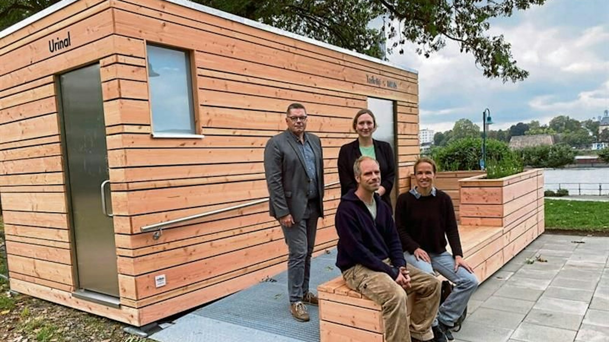 Vier Personen stehen und sitzen vor dem neuen Toilettenhäuschen.