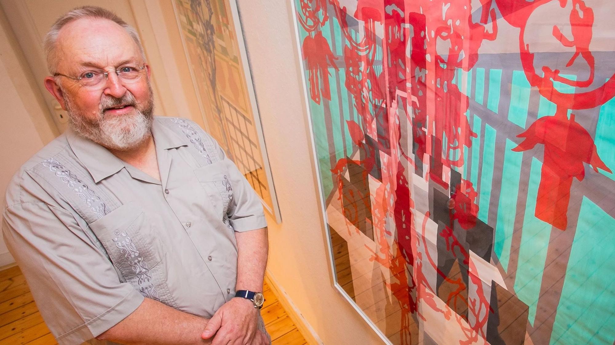 Im Bild ist ein Künstler vor einem seiner Bilder.