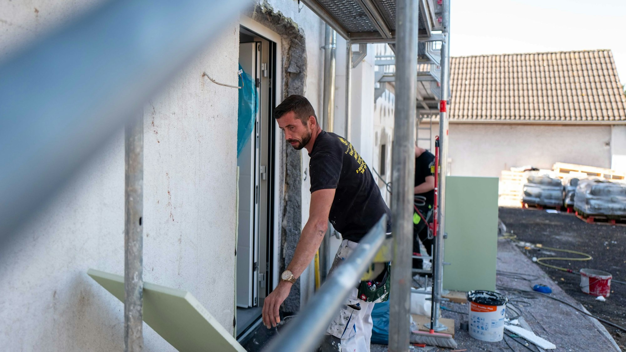 Das Bild zeigt einen Handwerker, wie er im Außenbereich unter einem Grüst hantiert.