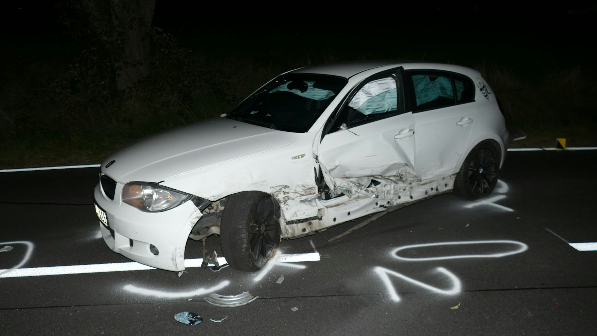 Ein zerbeultes Auto steht nachts auf de Straße.