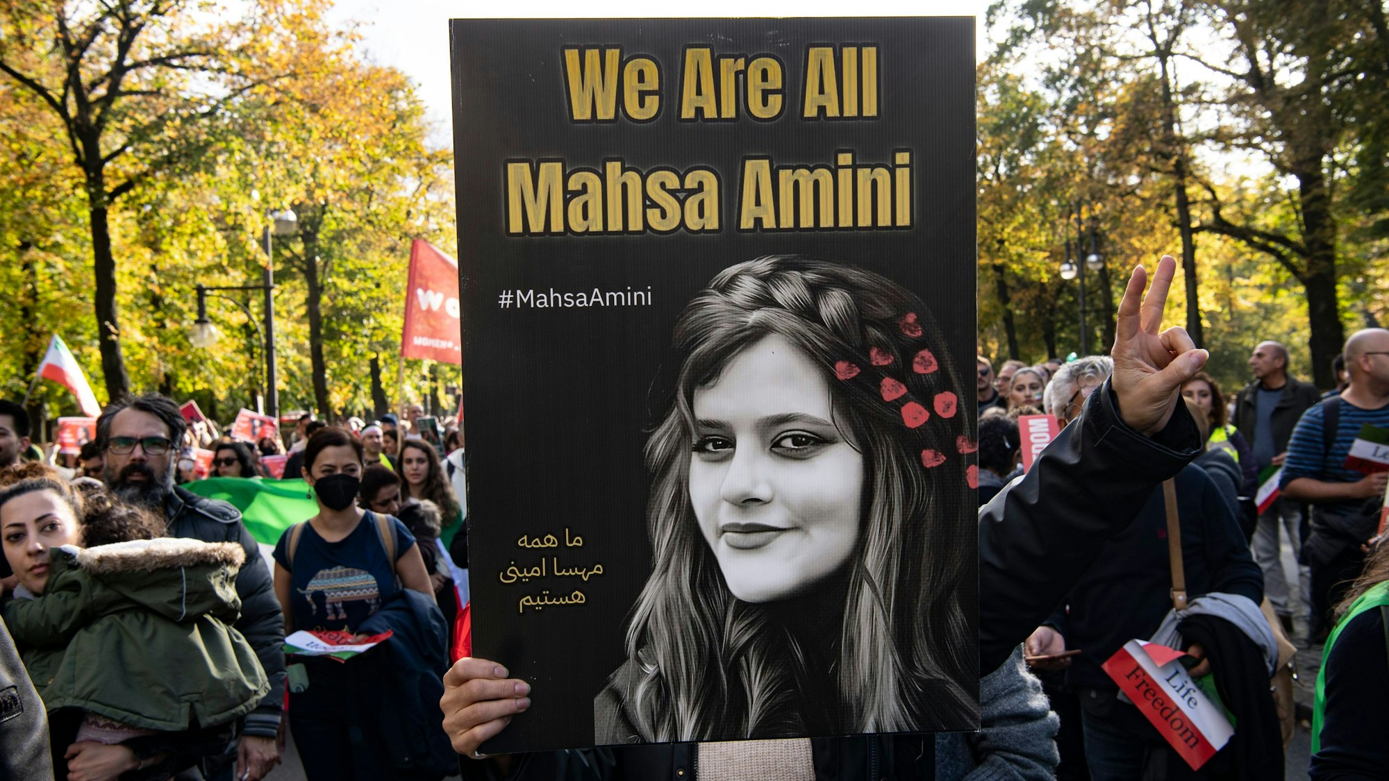Ein Teilnehmer der Großdemonstration „Solidarität mit den Protestierenden im Iran“ hält am Großen Stern ein Plakat mit der Aufschrift ‚We Are All Mahsa Amini‘ hoch. (Archivbild aus 2022).