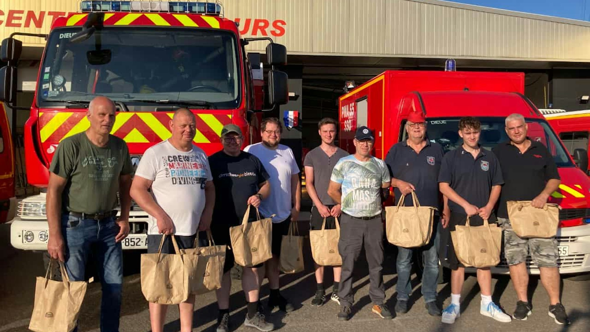 Feuerwehrleute aus Overath stehen mit ihren Gastgebern vor Feuerwehrfahrzeugen in Dieue sur Meuse.