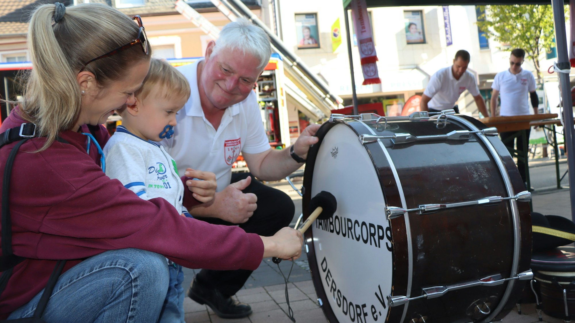 Mutter und Sohn knien vor der großen Trommel eines Musikers.