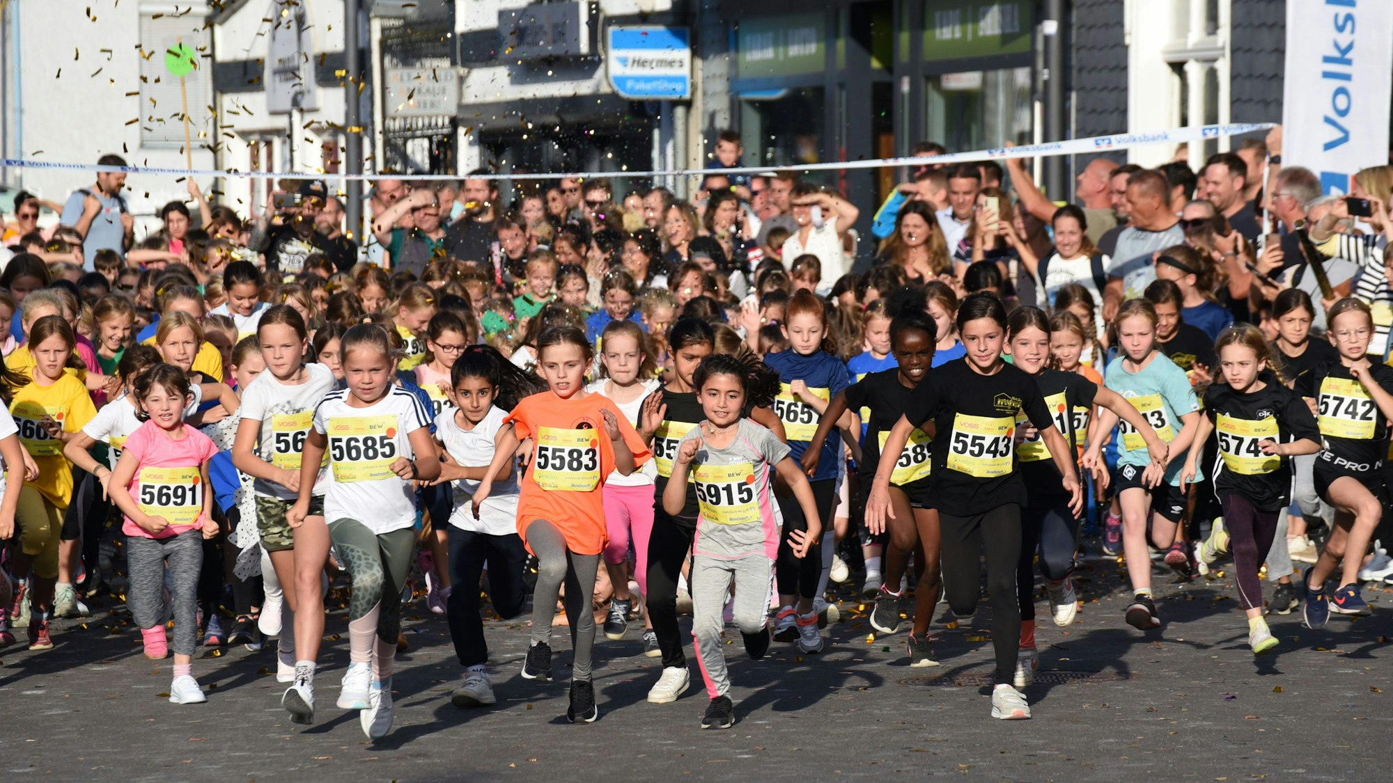 Zahlreiche Kinder starten unter Konfettiregen bei einem Stadtlauf an der Ziellinie.