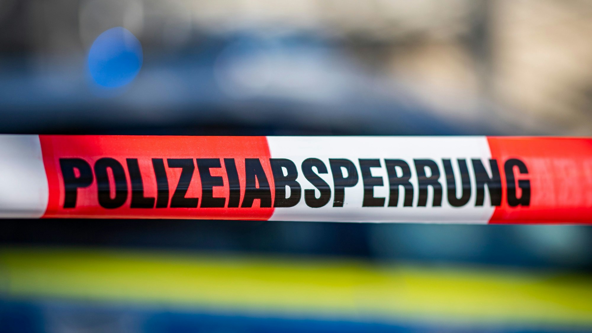 Ein Absperrband mit der Aufschrift „Polizeiabsperrung“ ist vor einem Polizeiwagen aufgespannt. (Symbolbild)