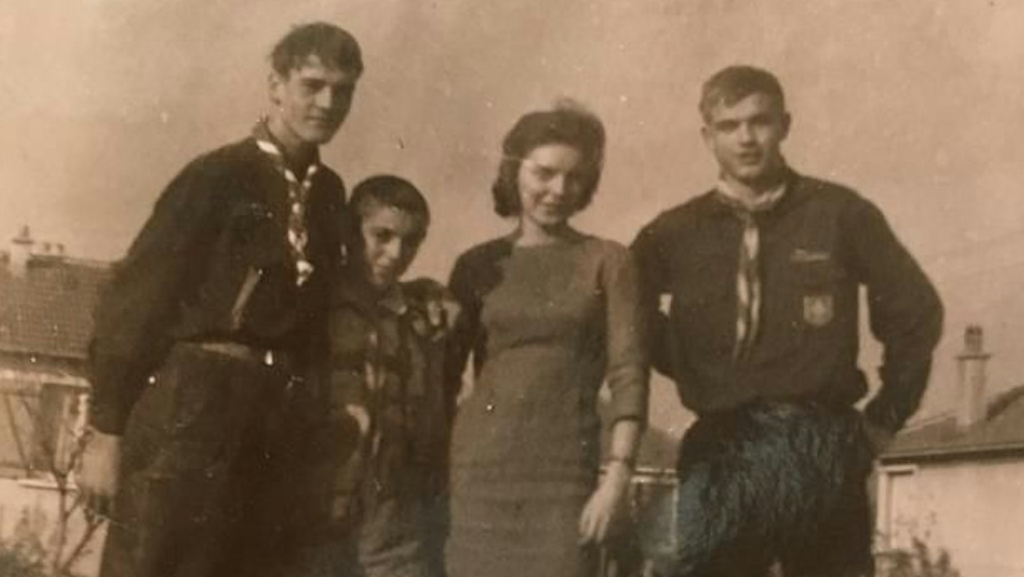 Zwei Pfadfinder stehen mit einer Frau und einem Kind vor Häusern.