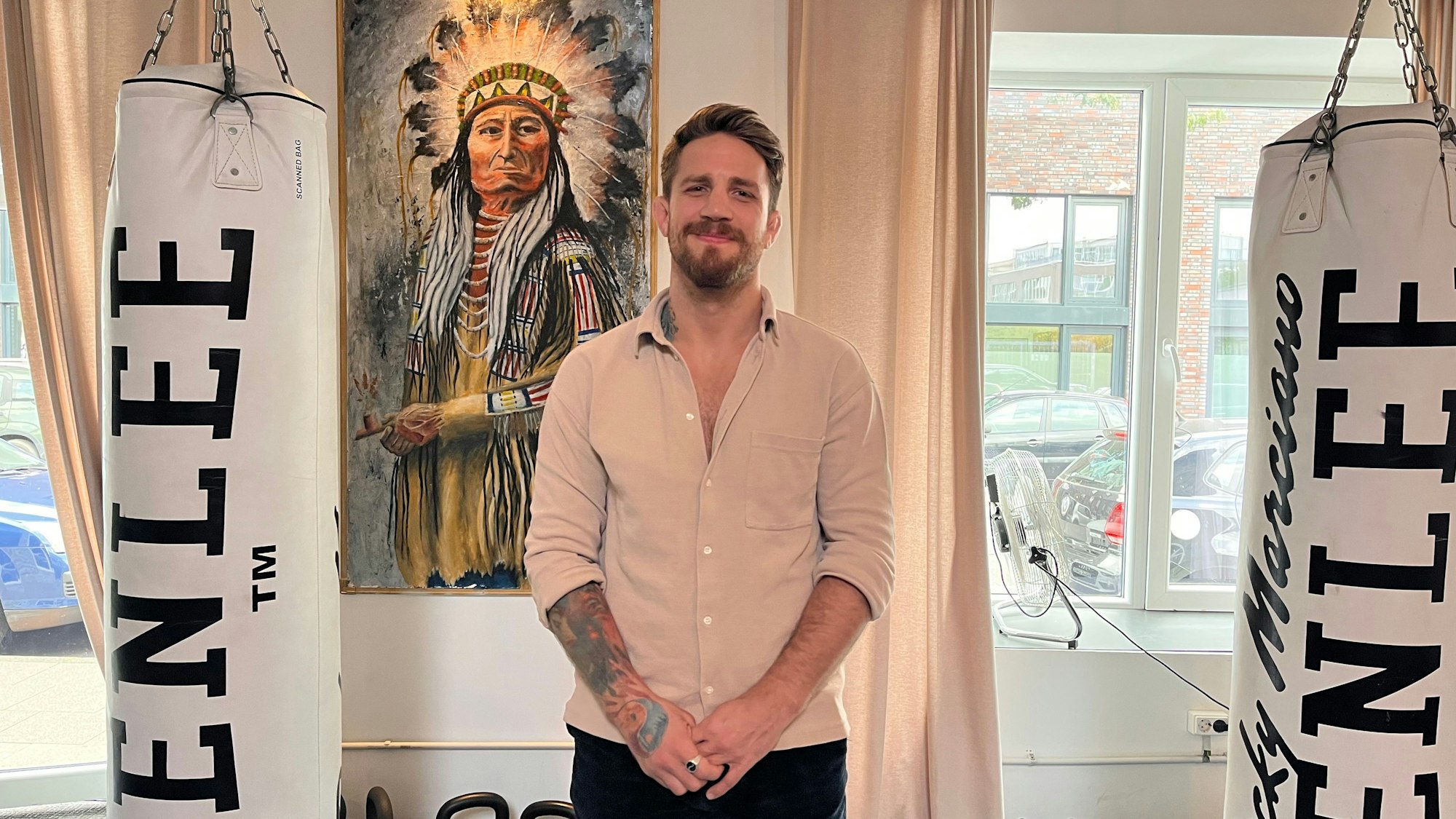 Ein Mann mit Bart steht vor einem Bild von einem Indianerhäuptling.