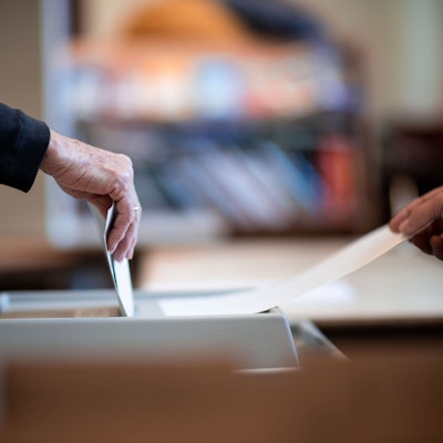 Eine Person wirft einen versiegelten Wahlzettel in eine Wahlurne.