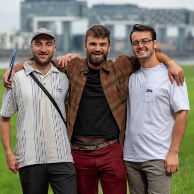 Andreas Stickelmann, Simon Heuser und Leonard Träger stehen auf den Poller Wiesen, im Hintergrund die Kranhäuser.