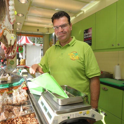 Ein Mann im grünen Poloshirt steht hinter einer Verkaufstheke mit gebrannten Mandeln.
