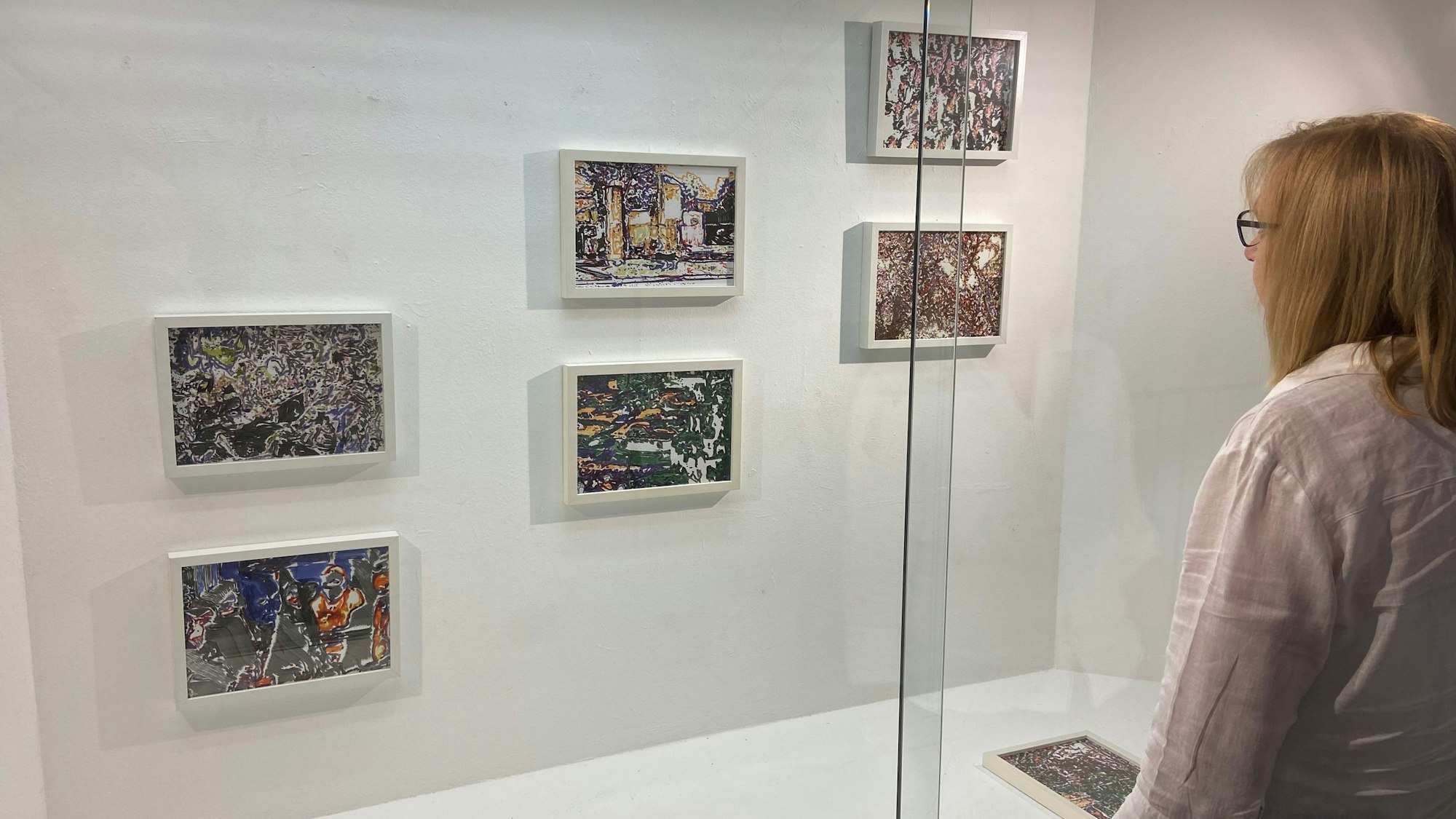 Eine Frau betrachtet kleinformatige Bilder, die an einer Wand hängen.