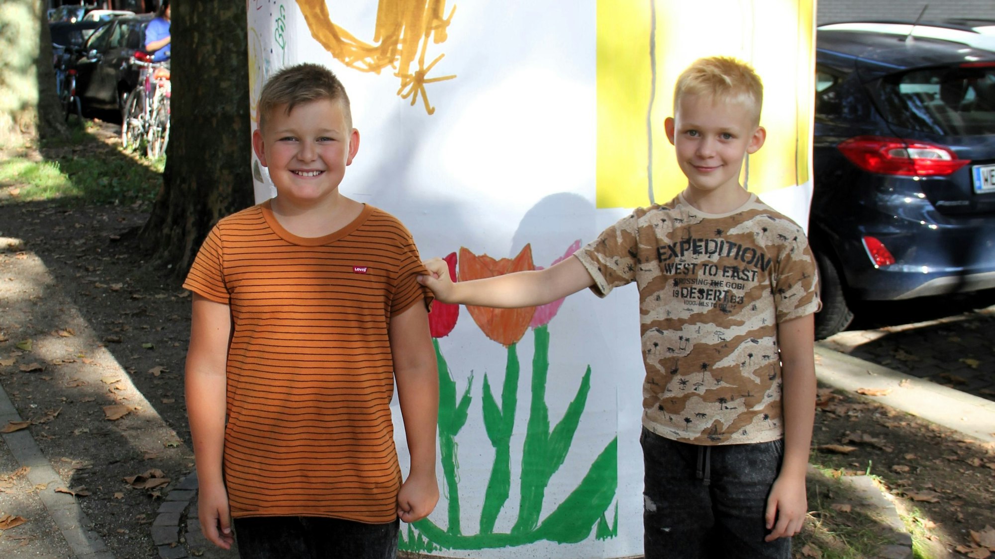 Zwei zehnjährige Jungs stehen vor einer bunt bemalten Litfaßsäule.