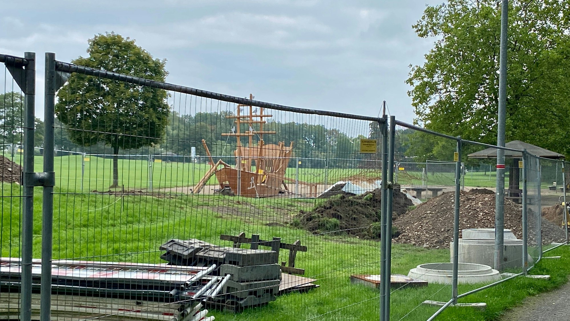 Zu sehen ist eine umzäunte Wiese, auf der Baumaterial lagert.