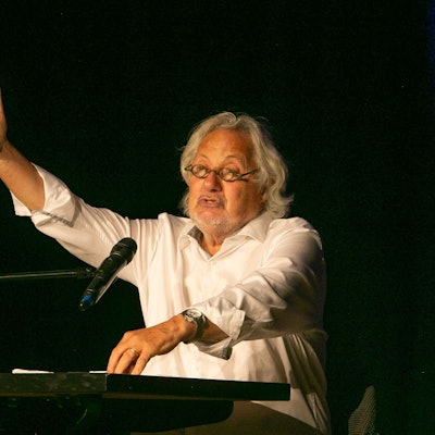 Der Kabarettist Konrad Beikircher sitzt gestikulierend an einem Tisch, vor ihm ein Glas Weißwein.