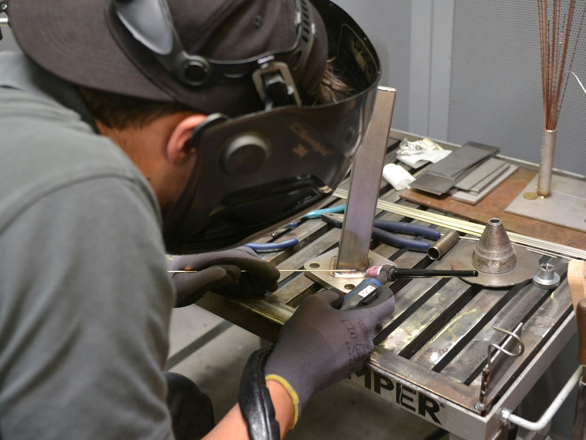 Ein junger Geselle ist von hinten zu sehen. Er trägt eine Schutzbrille und demonstriert, worauf es in seinem Beruf im Metallbau ankommt.