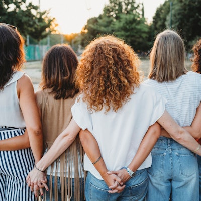 Eine Gruppe Freundinnen hält hinter dem Rücken Händchen.