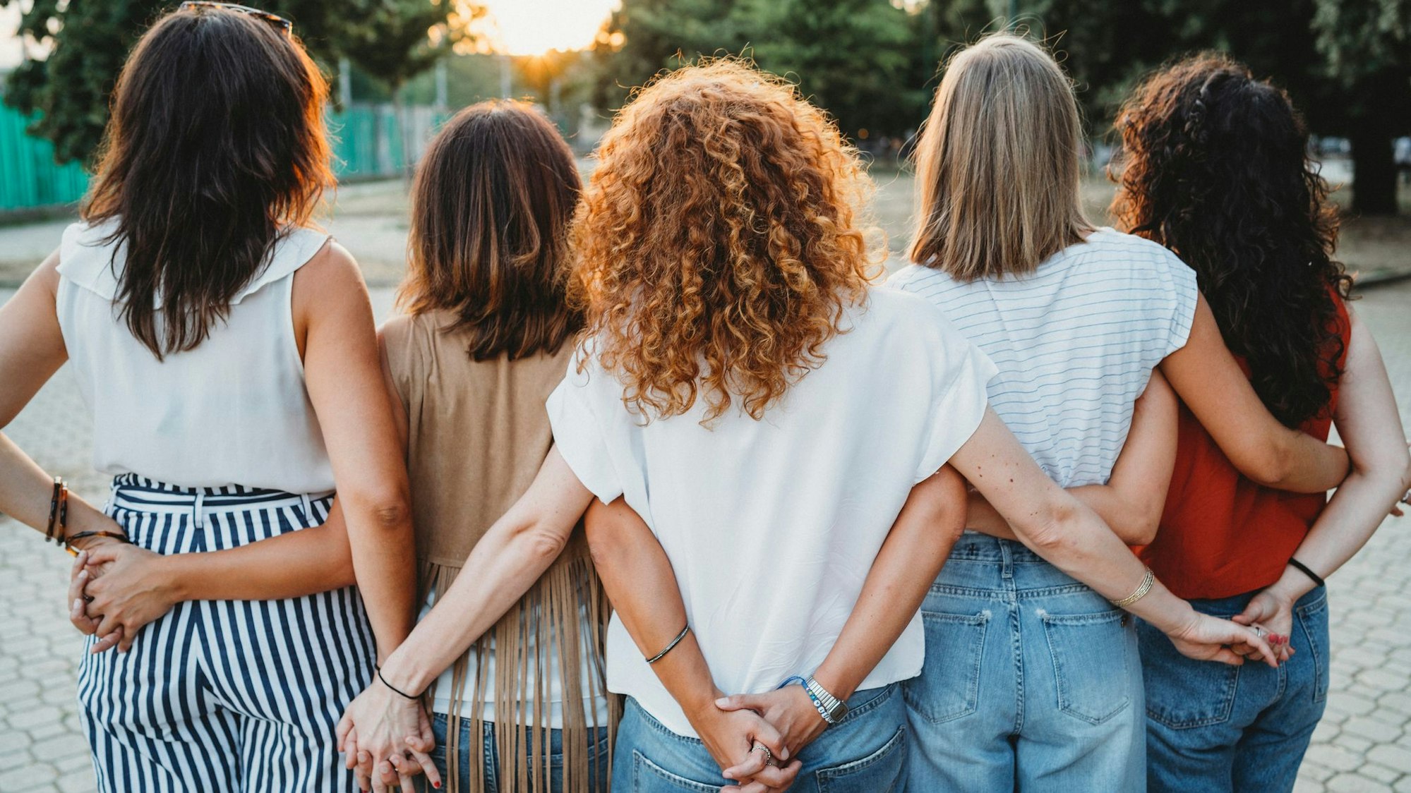 Eine Gruppe Freundinnen hält hinter dem Rücken Händchen.