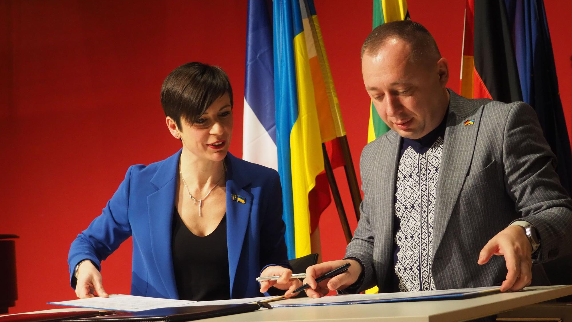 Eine Frau und ein Mann unterschreiben auf einem Pult eine Urkunde.