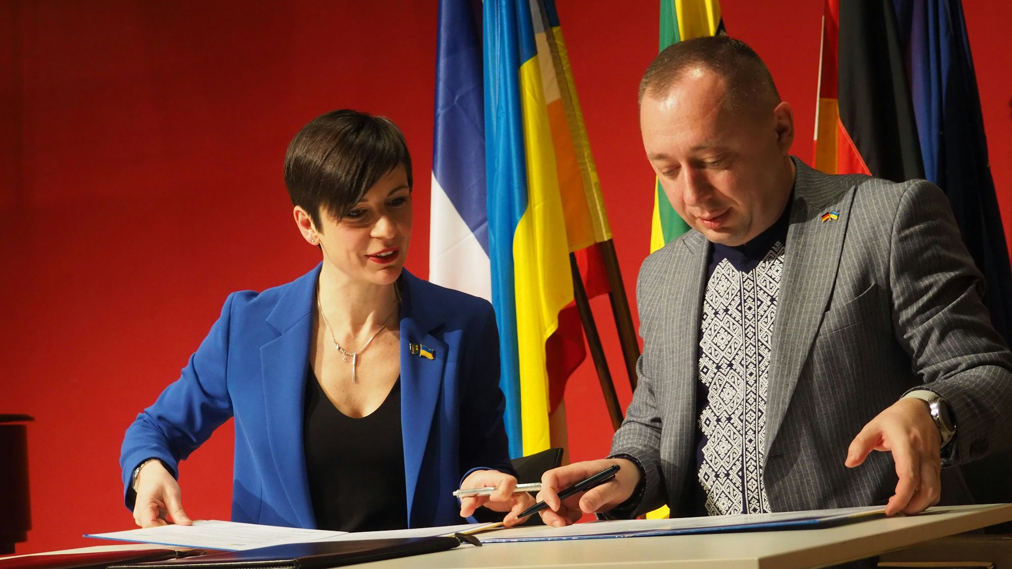 Eine Frau und ein Mann unterschreiben auf einem Pult eine Urkunde.