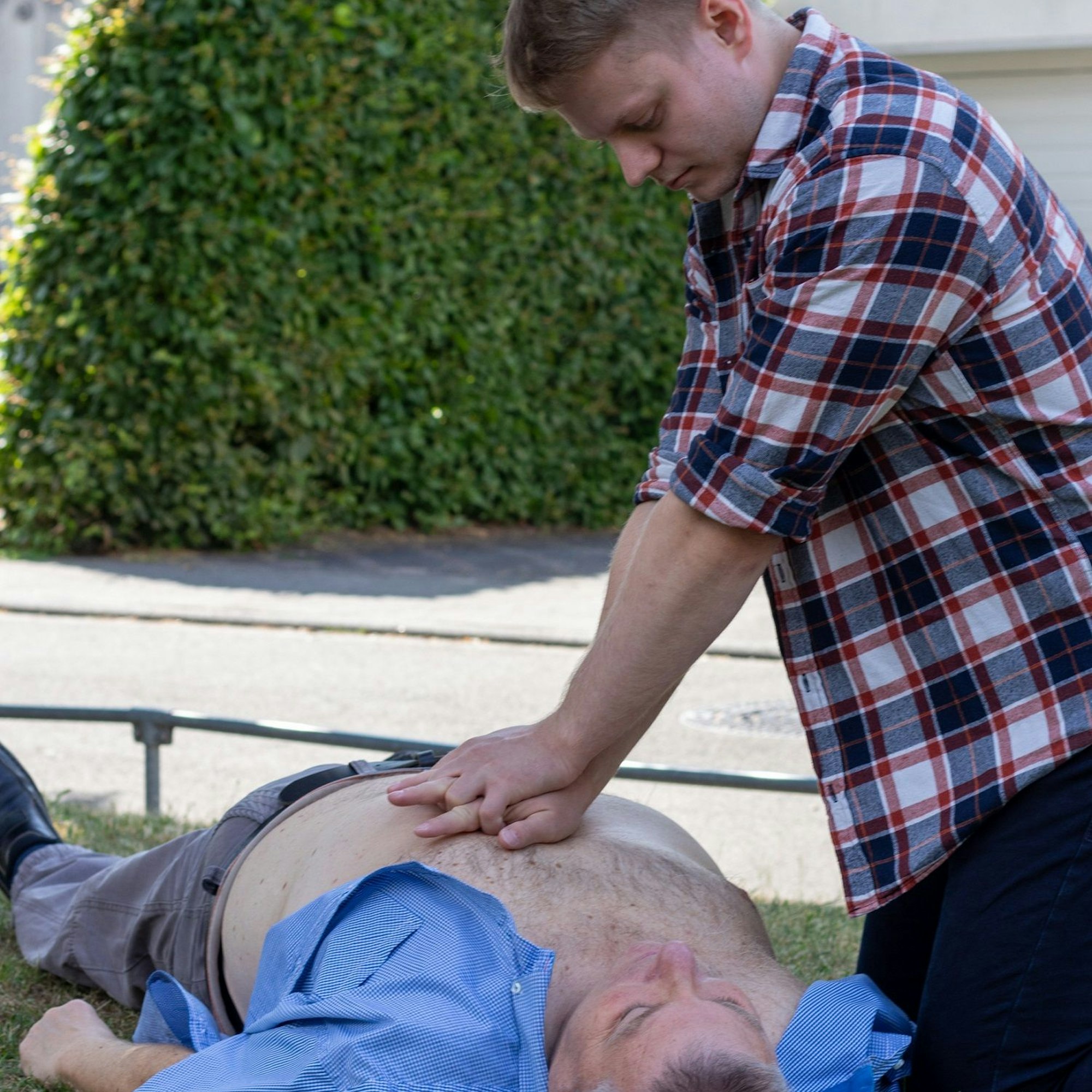 Ein Ersthelfer nimmt eine Herz-Druckmassage bei einem Patienten auf einer Rasenfläche vor.